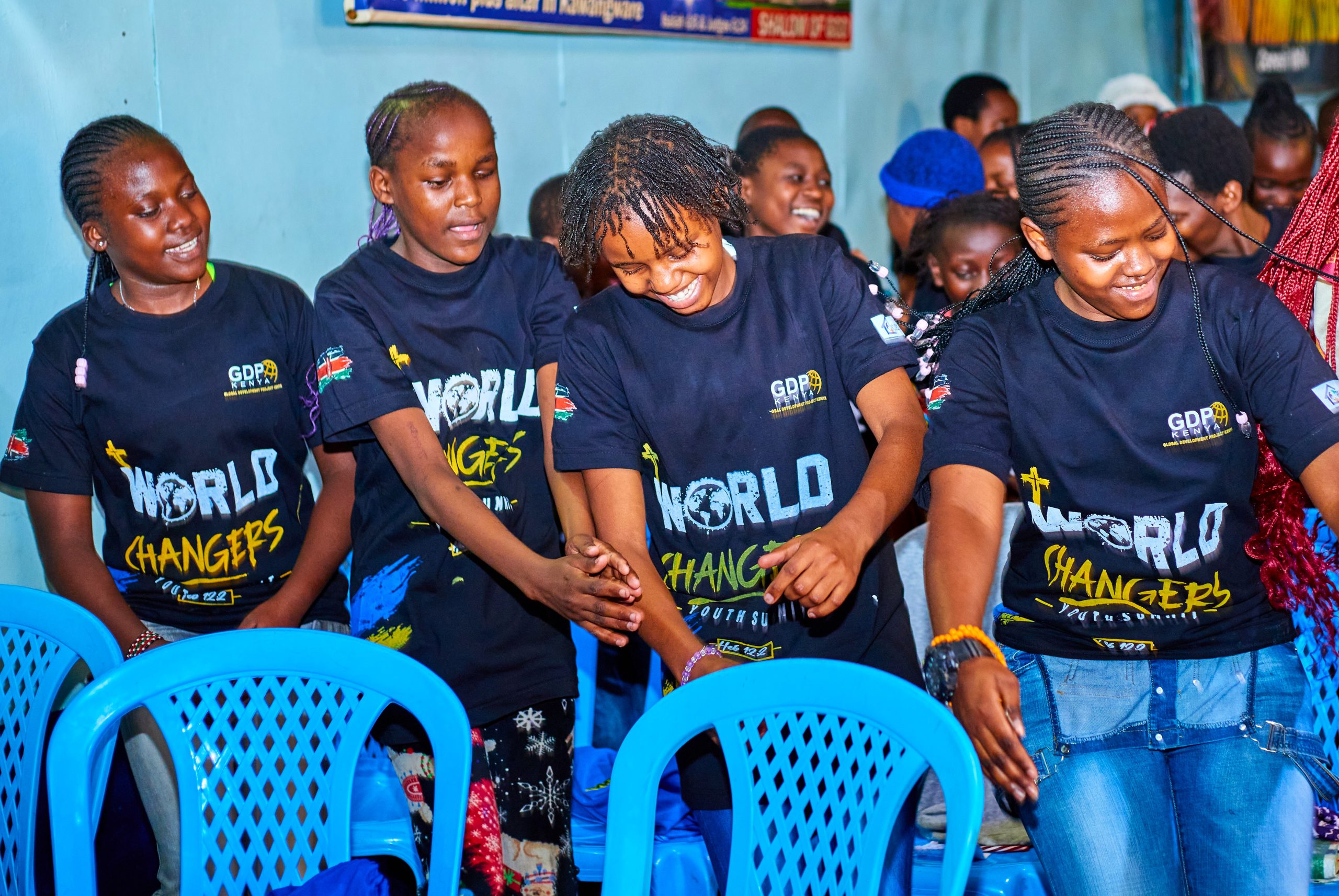 Girls in GDP Kenya World Changers shirts laughing together, hands linked during a summit session