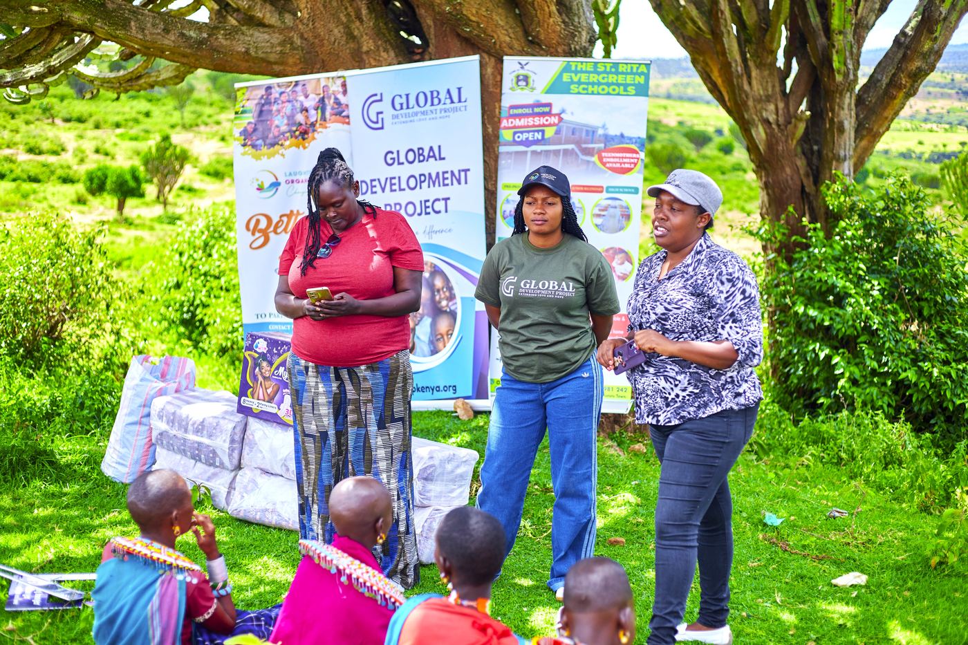 GDP Kenya staff briefing the community under a tree, with St. Rita and GDP banners