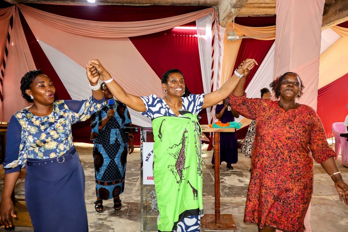 Three women celebrating with raised, joined hands at a GDP women's gathering in Kenya