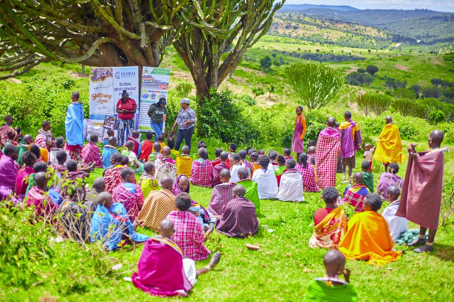 GDP Samburu Project outdoor community session — GDP banner, hundreds of Samburu women in colorful traditional dress seated on green hillside, Northern Kenya 2026