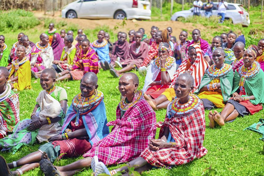 Samburu community elders seated on grass listening at GDP event — beaded necklaces, traditional dress, Northern Kenya