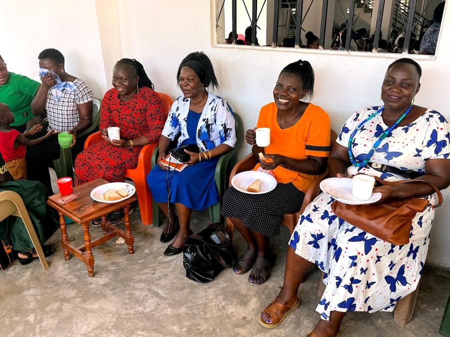 Four women holding cups of tea and food plates, colorful dresses, smiling at GDP Women's Empowerment conference