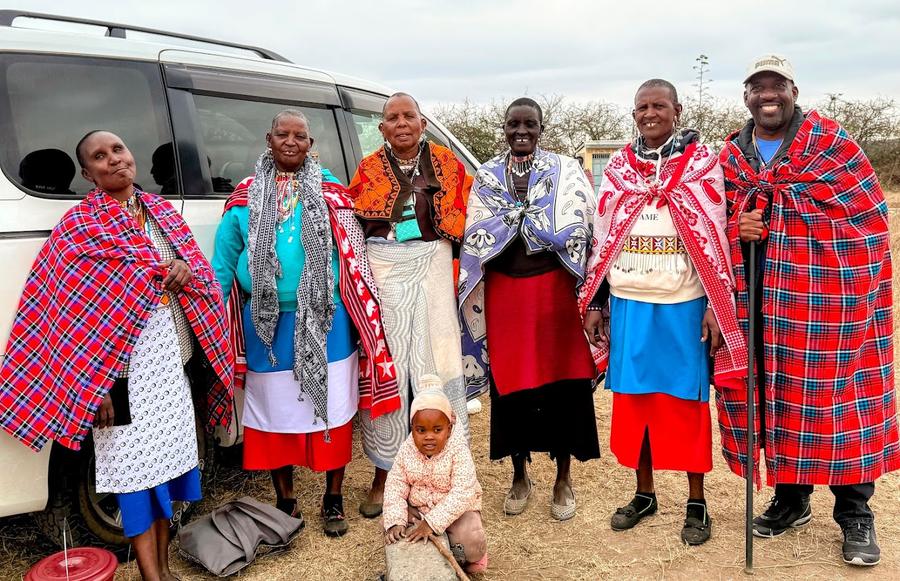 Maasai community members with GDP vehicle — humanitarian visit, traditional red plaid dress and beaded jewelry, Kenya